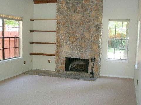 unfurnished living room with a stone fireplace, carpet floors, and plenty of natural light