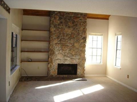 unfurnished living room featuring beamed ceiling, carpet flooring, and a fireplace