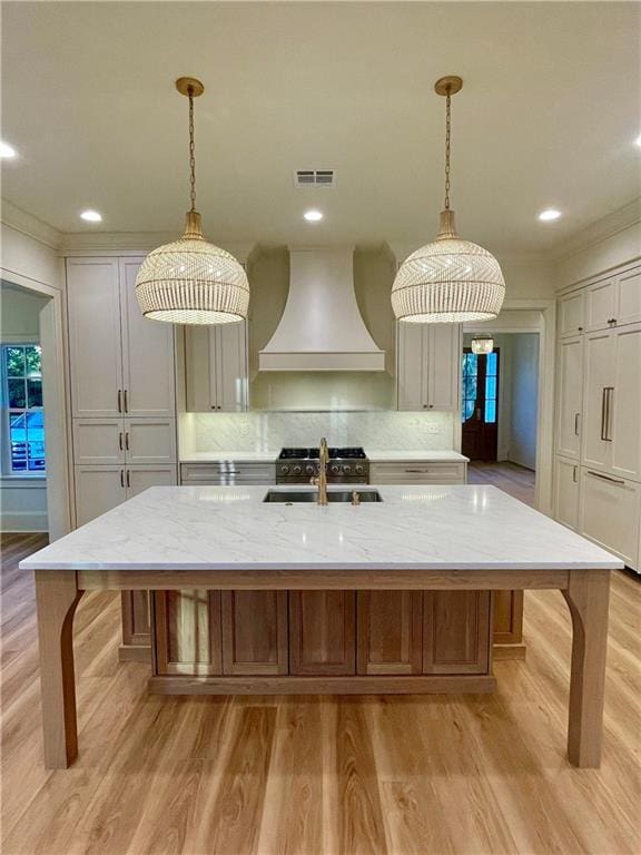 kitchen with a large island, light stone counters, decorative light fixtures, and custom exhaust hood