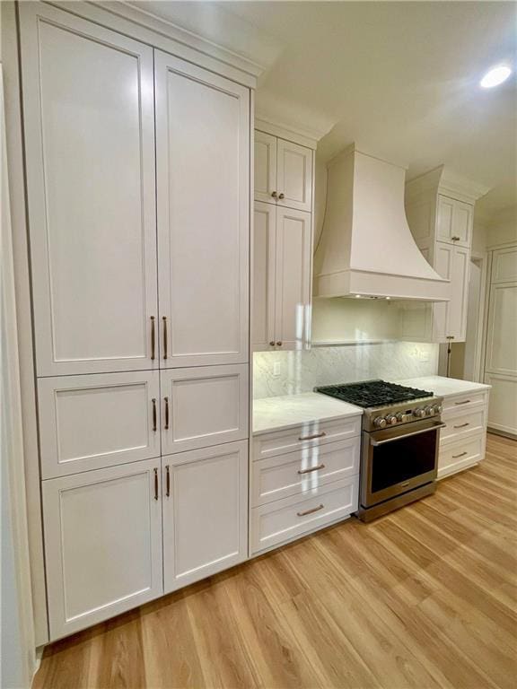 kitchen with custom exhaust hood, white cabinets, stainless steel range, and light hardwood / wood-style flooring