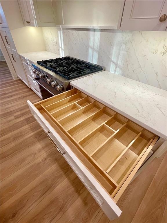 details featuring white cabinetry, stainless steel range, decorative backsplash, and light wood-type flooring