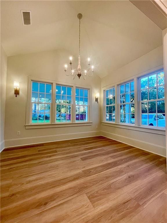 unfurnished dining area with wood-type flooring, a chandelier, and vaulted ceiling