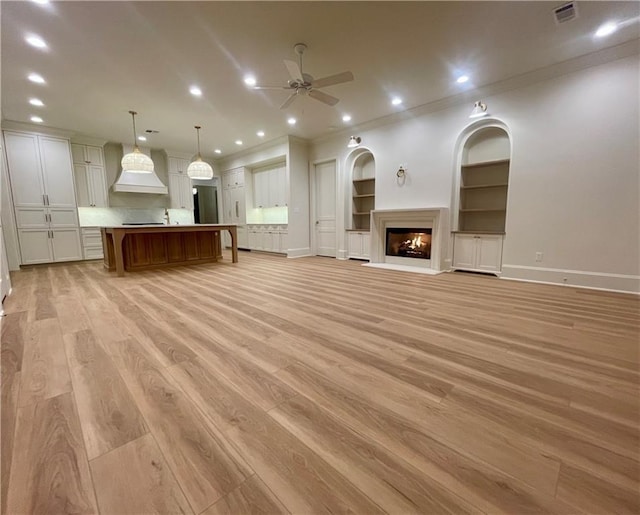 unfurnished living room featuring ceiling fan, ornamental molding, light hardwood / wood-style flooring, and built in features