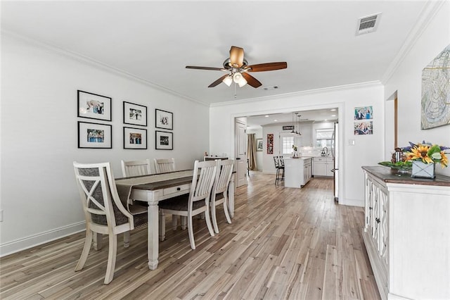 dining space with ceiling fan, ornamental molding, sink, and light wood-type flooring