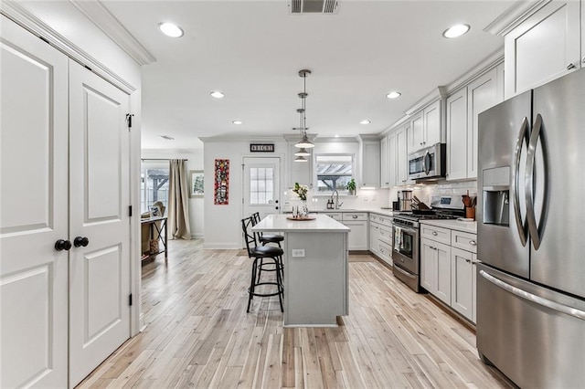 kitchen featuring hanging light fixtures, a kitchen breakfast bar, stainless steel appliances, a center island, and light wood-type flooring