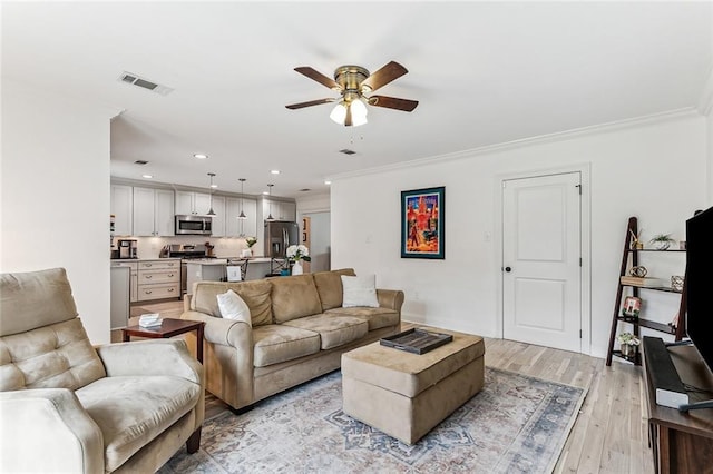 living room with ornamental molding, light hardwood / wood-style floors, and ceiling fan