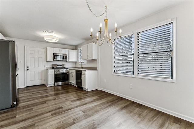 kitchen featuring pendant lighting, dark wood-type flooring, stainless steel appliances, a notable chandelier, and white cabinets