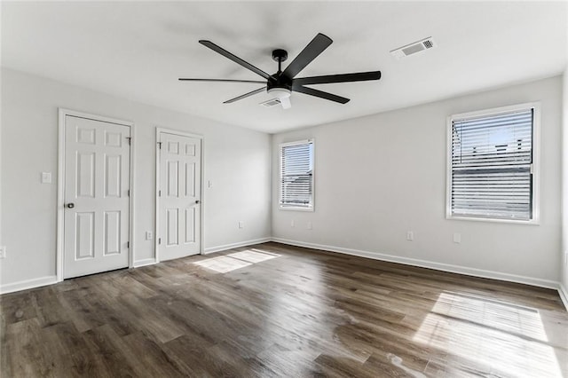 unfurnished bedroom with ceiling fan, dark hardwood / wood-style floors, and two closets