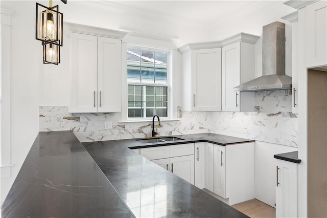 kitchen with decorative light fixtures, white cabinetry, sink, and wall chimney exhaust hood