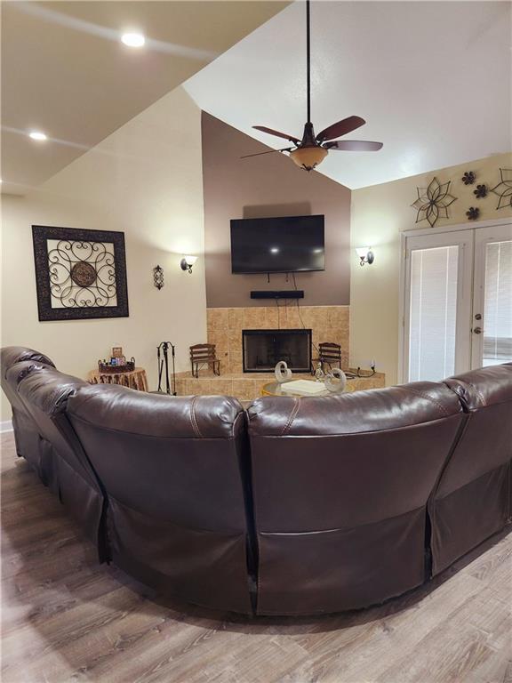 living room featuring hardwood / wood-style flooring, ceiling fan, high vaulted ceiling, a fireplace, and french doors