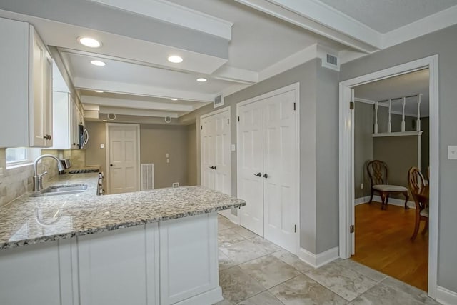 kitchen with tasteful backsplash, white cabinets, light stone counters, kitchen peninsula, and beam ceiling