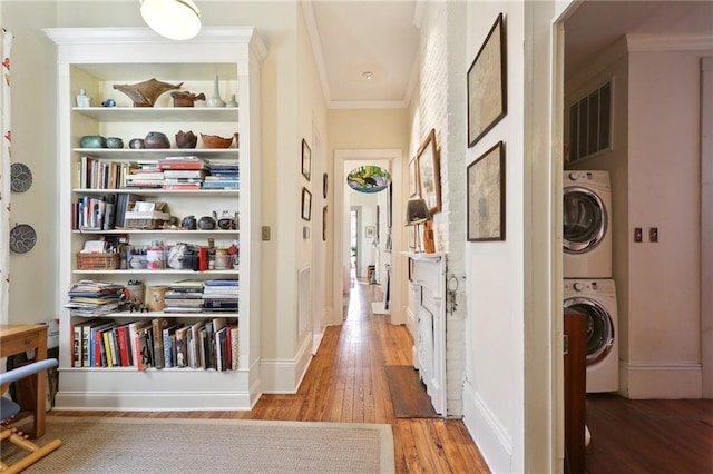 hall featuring stacked washer / dryer, ornamental molding, and light hardwood / wood-style floors