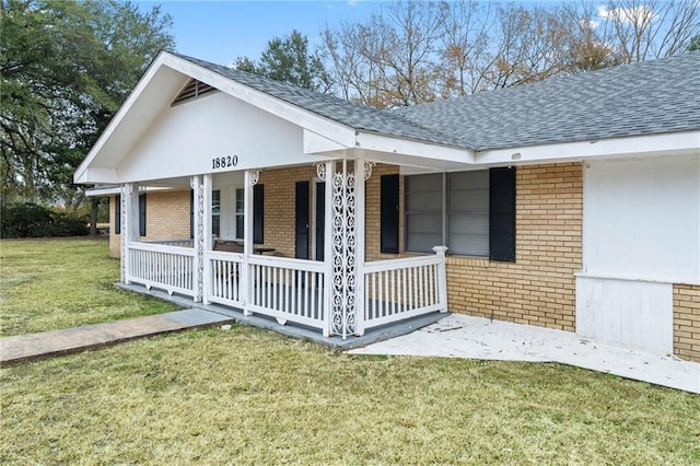 view of side of property featuring a yard, a porch, roof with shingles, and brick siding