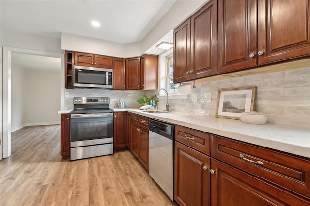 kitchen featuring sink, appliances with stainless steel finishes, light stone countertops, decorative backsplash, and light wood-type flooring