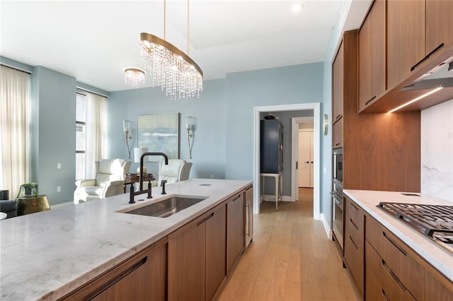 kitchen with appliances with stainless steel finishes, decorative light fixtures, tasteful backsplash, sink, and light wood-type flooring