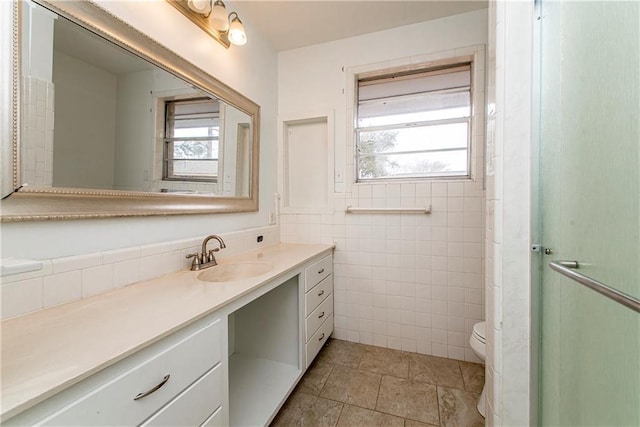 bathroom with tile walls, vanity, toilet, and a healthy amount of sunlight