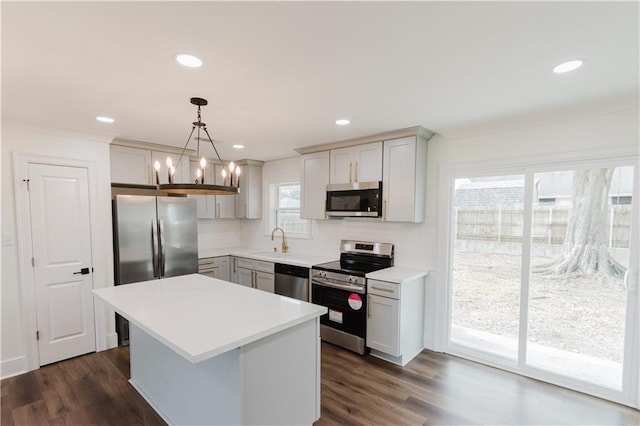 kitchen featuring dark wood-type flooring, sink, hanging light fixtures, appliances with stainless steel finishes, and a kitchen island