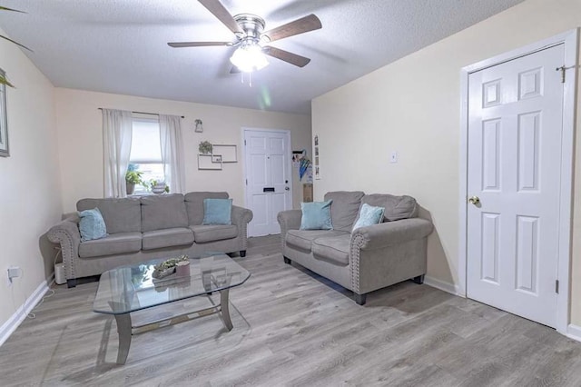 living room with ceiling fan, a textured ceiling, and light wood-type flooring