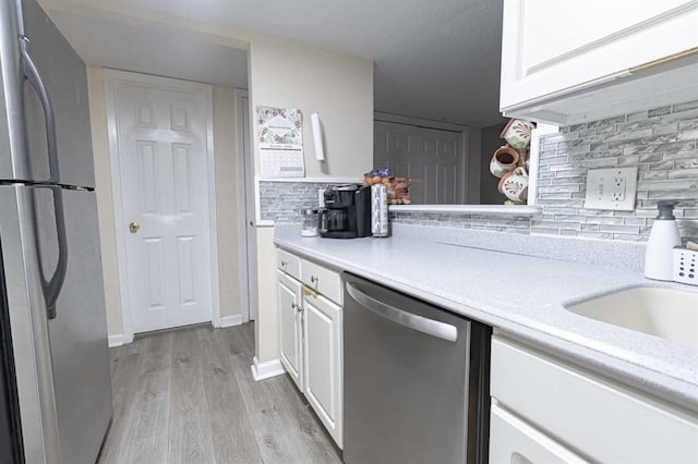 kitchen featuring backsplash, stainless steel appliances, light hardwood / wood-style floors, and white cabinets