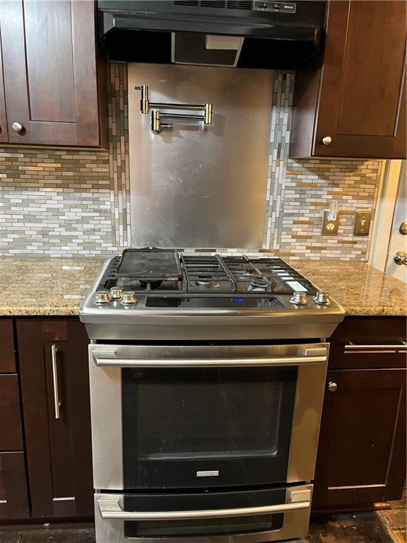 kitchen with light stone counters, gas range, tasteful backsplash, and dark brown cabinetry