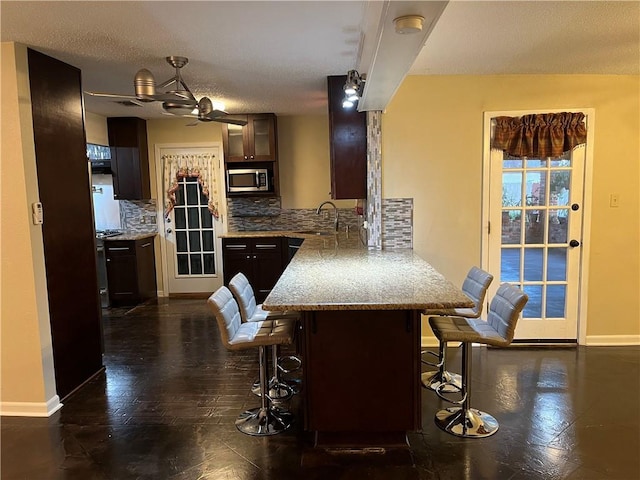 kitchen featuring sink, a kitchen breakfast bar, decorative backsplash, light stone countertops, and dark brown cabinets