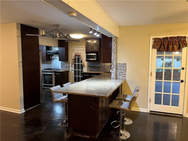 kitchen featuring a breakfast bar area, appliances with stainless steel finishes, dark brown cabinets, decorative backsplash, and kitchen peninsula