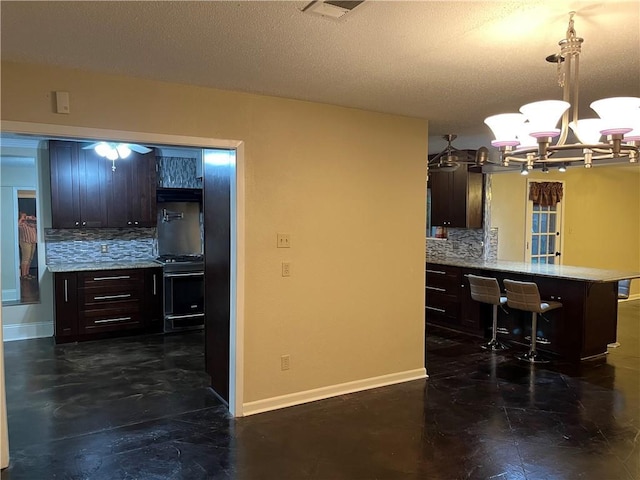 kitchen with a kitchen bar, gas stove, hanging light fixtures, kitchen peninsula, and backsplash