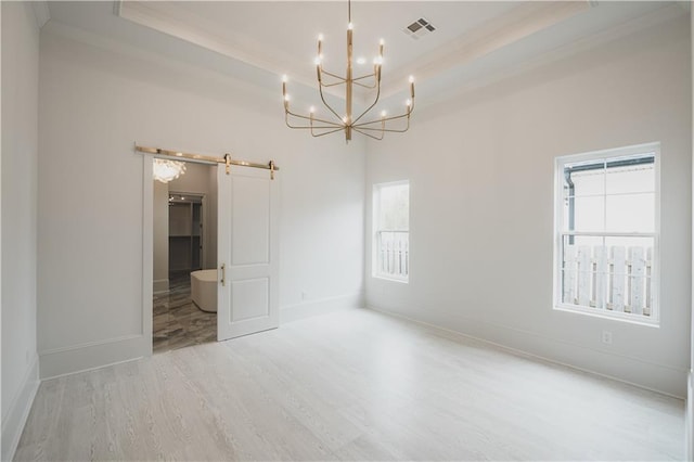 empty room with a barn door, a notable chandelier, a tray ceiling, and hardwood / wood-style flooring