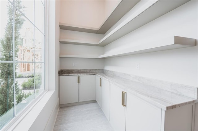 bar featuring light stone countertops, light hardwood / wood-style floors, and white cabinets