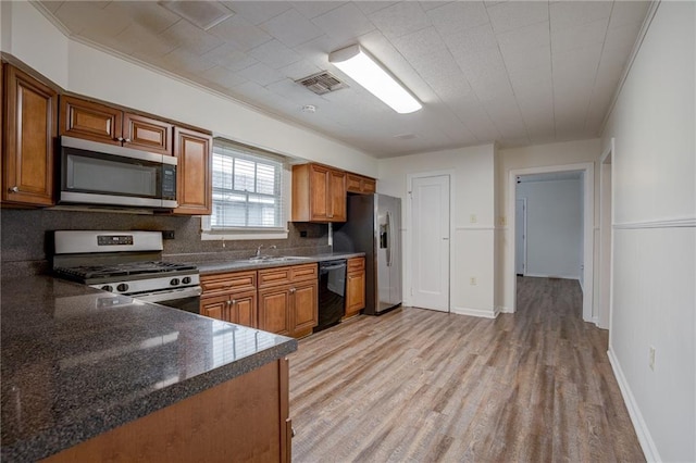 kitchen with tasteful backsplash, sink, dark stone counters, stainless steel appliances, and light wood-type flooring