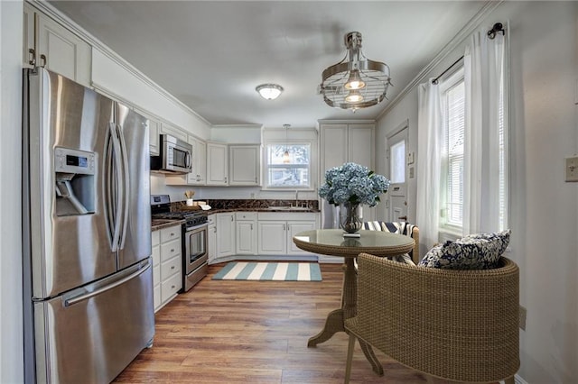 kitchen with decorative light fixtures, white cabinets, ornamental molding, stainless steel appliances, and light hardwood / wood-style flooring