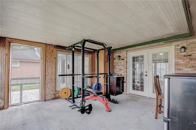 workout area featuring washer / dryer, french doors, a healthy amount of sunlight, and brick wall