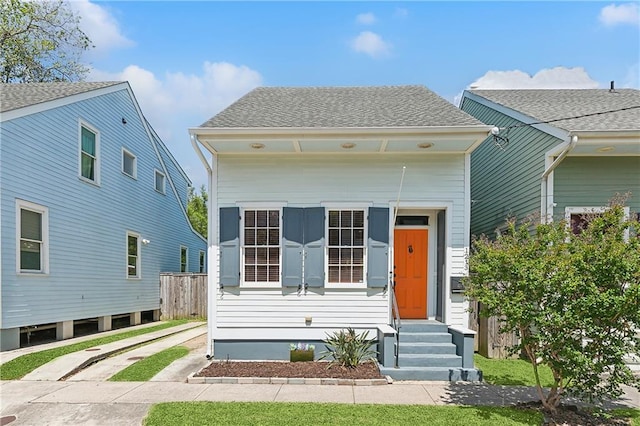 shotgun-style home with entry steps, a shingled roof, and fence