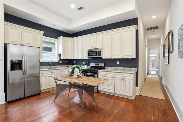 kitchen with dark wood-type flooring, stainless steel appliances, light stone countertops, and sink