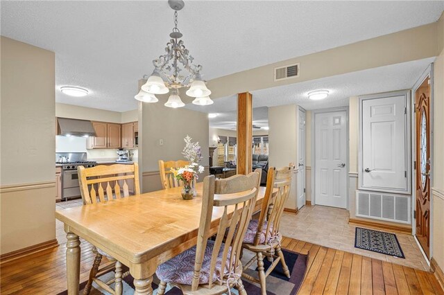 dining space with an inviting chandelier, light hardwood / wood-style floors, and a textured ceiling