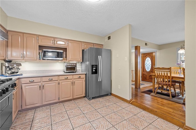 kitchen with stainless steel appliances, light brown cabinets, a textured ceiling, and light wood-type flooring