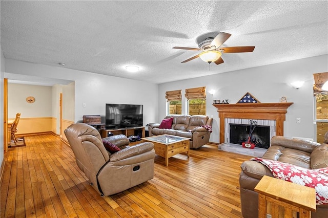 living room featuring a textured ceiling, a fireplace, light hardwood / wood-style floors, and ceiling fan