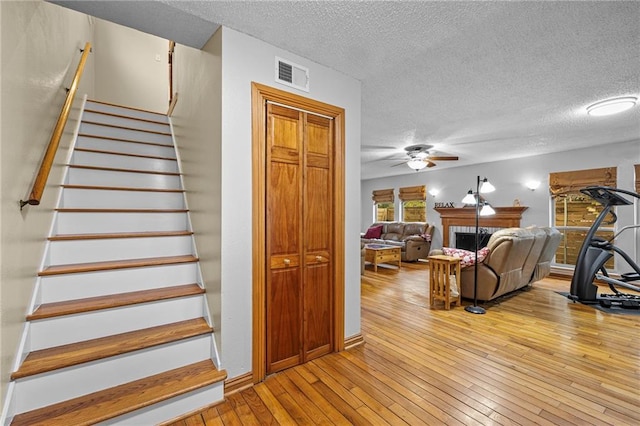 stairway with ceiling fan, a textured ceiling, a fireplace, wood finished floors, and visible vents