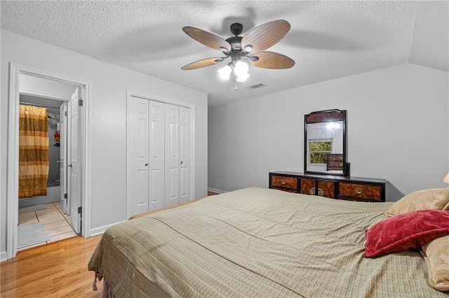 bedroom with a textured ceiling, wood finished floors, visible vents, vaulted ceiling, and a closet