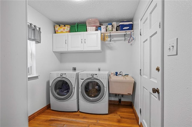 washroom with sink, cabinets, a textured ceiling, washer and clothes dryer, and light hardwood / wood-style floors