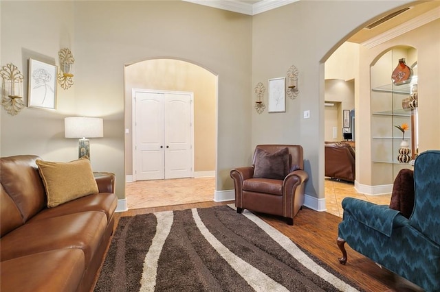 living room with a towering ceiling, ornamental molding, and light wood-type flooring