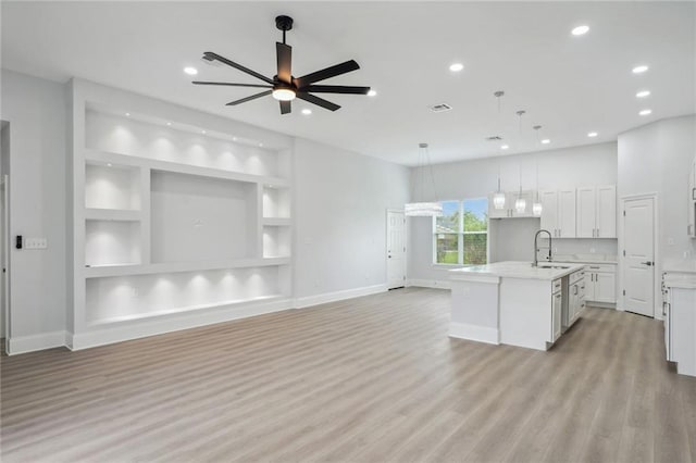 kitchen with light wood-type flooring, an island with sink, light countertops, white cabinetry, and open floor plan