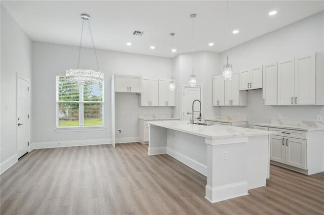 kitchen with visible vents, a kitchen island with sink, a sink, white cabinets, and light wood-style floors