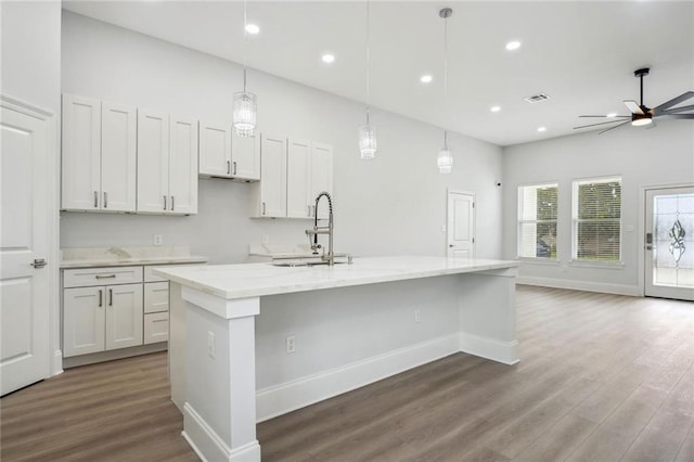 kitchen with light stone counters, wood finished floors, a spacious island, recessed lighting, and a sink