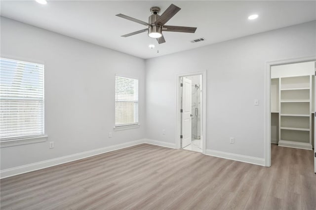 unfurnished bedroom featuring visible vents, baseboards, a walk in closet, and light wood-style flooring