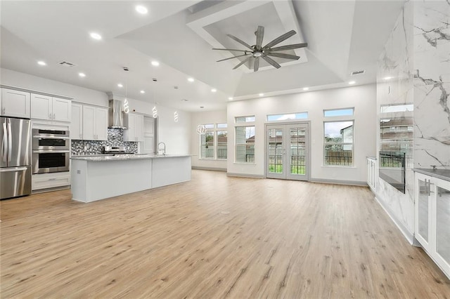 kitchen featuring white cabinetry, appliances with stainless steel finishes, pendant lighting, a kitchen island with sink, and wall chimney range hood