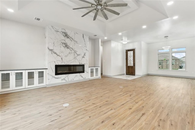 unfurnished living room with ceiling fan, a high end fireplace, a tray ceiling, and light hardwood / wood-style flooring