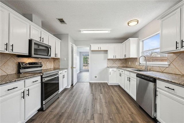 kitchen with stone countertops, stainless steel appliances, a sink, visible vents, and dark wood finished floors