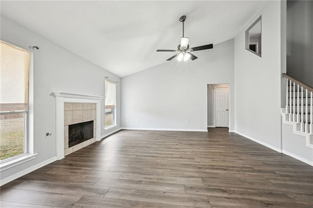 unfurnished living room featuring stairs, a fireplace, dark wood finished floors, and a wealth of natural light