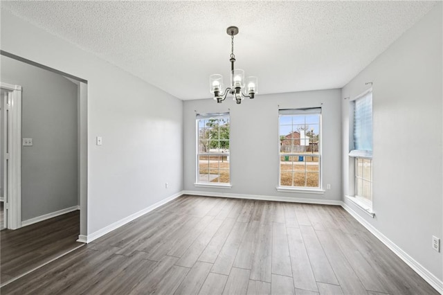 unfurnished dining area with dark wood-type flooring, a notable chandelier, and a textured ceiling